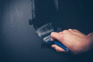 A person painting a wall black.